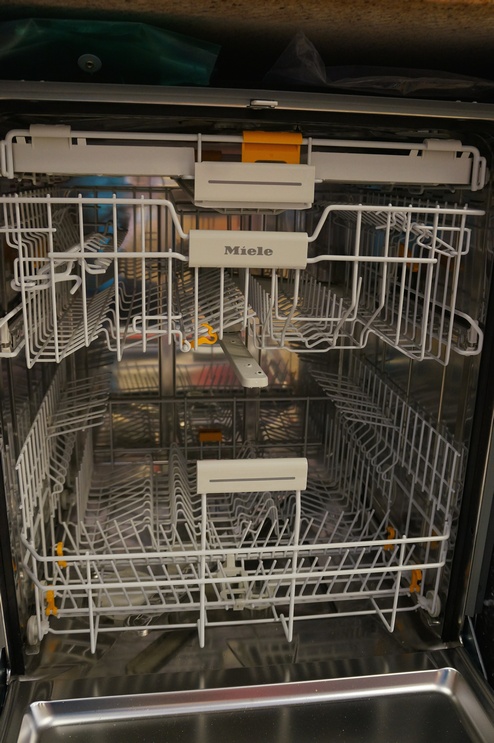 The dishwasher features a 3-tier rack system with Miele's FlexiCare Premium basket configuration and their 3D Cutlery Tray on top.